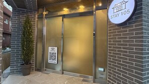 Entrada de hotel con diseño moderno, con puerta de vidrio, un letrero con un código QR y una pequeña planta en maceta.