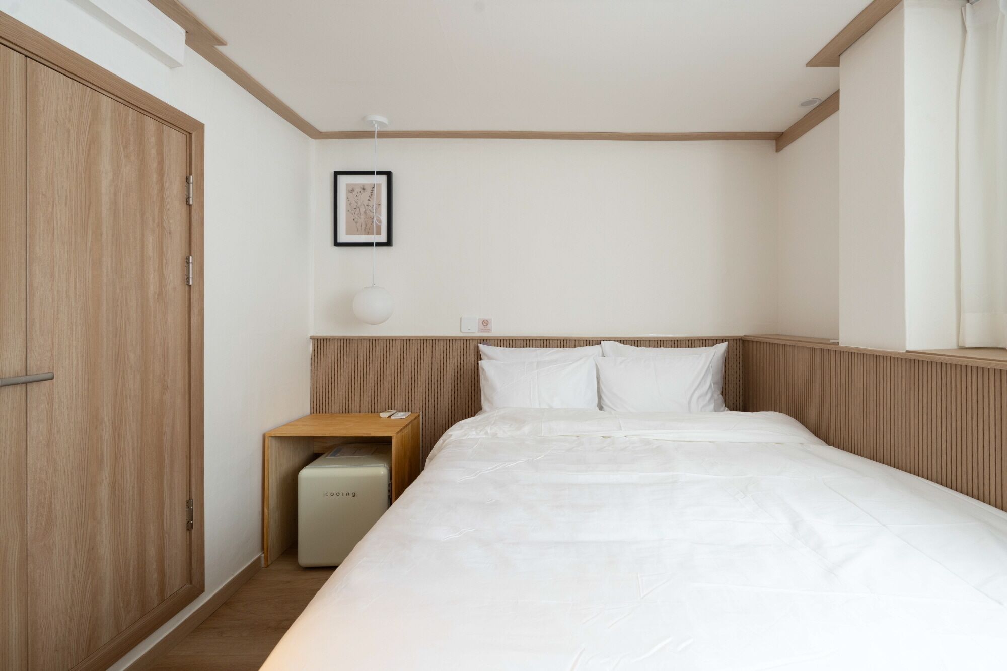 A bedroom with a bed, a nightstand, a bedside table, a framed picture, and a ceiling light.