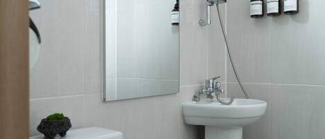 Un baño moderno con un lavabo blanco, un inodoro y una ducha. Hay tres botellas de champú en la pared.