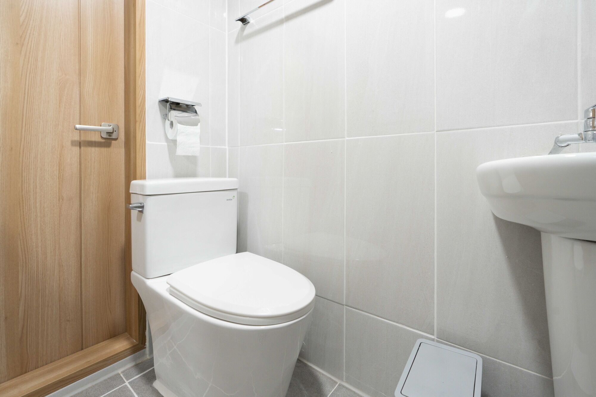 A modern bathroom with a toilet, a sink, and a wooden door.