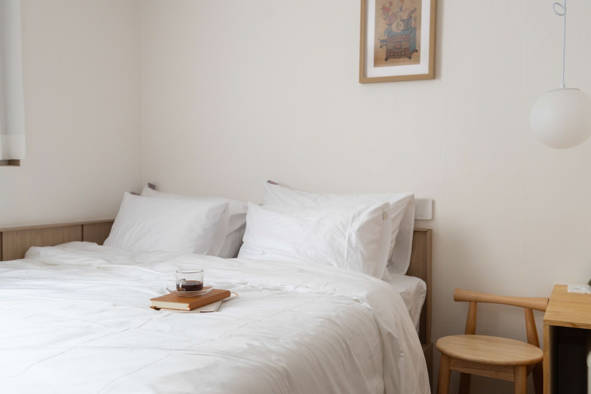 A neatly made bed with white linens, a glass of coffee, and a book on a wooden tray.
