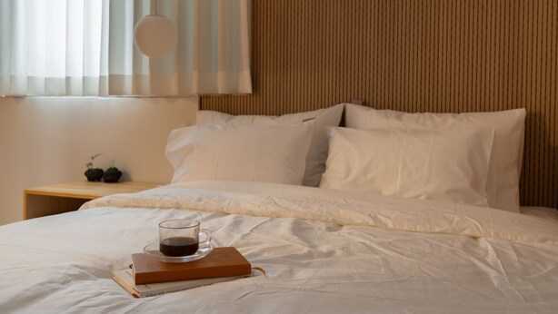 Una cama bien hecha con sábanas blancas, una taza de café en una bandeja y un libro a su lado.