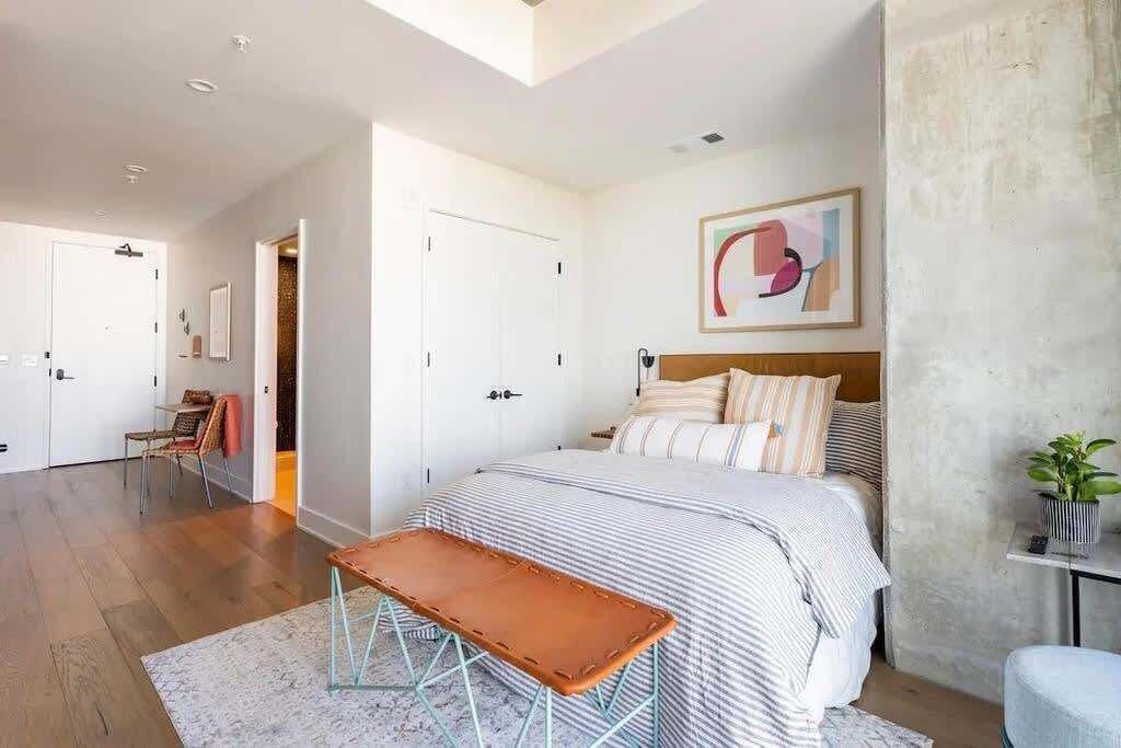 A bedroom with a large bed, a bench, a painting, and a view of the hallway.