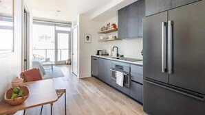A modern kitchen with dark cabinets, a stainless steel refrigerator, and a dining area with a table and chairs. - 🎶 Rainey St Studio with Rooftop Pool + Skyline Views | Natiivo Honor 🌇 (Austin)