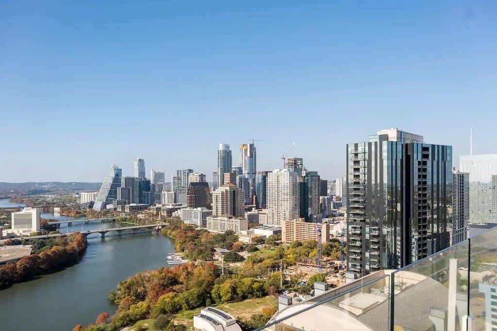 A city skyline with modern high-rise buildings, a river, and a bridge.