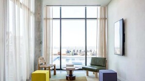 A modern living room with a large window, a flat-screen TV, and a view of a pool and cityscape. - 🎶 Rainey St Studio with Rooftop Pool + Skyline Views | Natiivo Honor 🌇 (Austin)