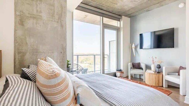 A modern bedroom with a large bed, a flat-screen TV mounted on the wall, and a balcony with a view. - 🎶 Rainey St Studio with Rooftop Pool + Skyline Views | Natiivo Honor 🌇 (Austin)