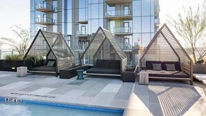 A rooftop pool area with three wooden structures, a modern building in the background, and a clear sky. - 🎶 Rainey St Studio with Rooftop Pool + Skyline Views | Natiivo Honor 🌇 (Austin)
