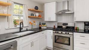 A modern kitchen with white cabinets, a black countertop, stainless steel appliances, and a window with curtains. - Walkable, Prime E. Austin Location - Casa Cherico (Austin)