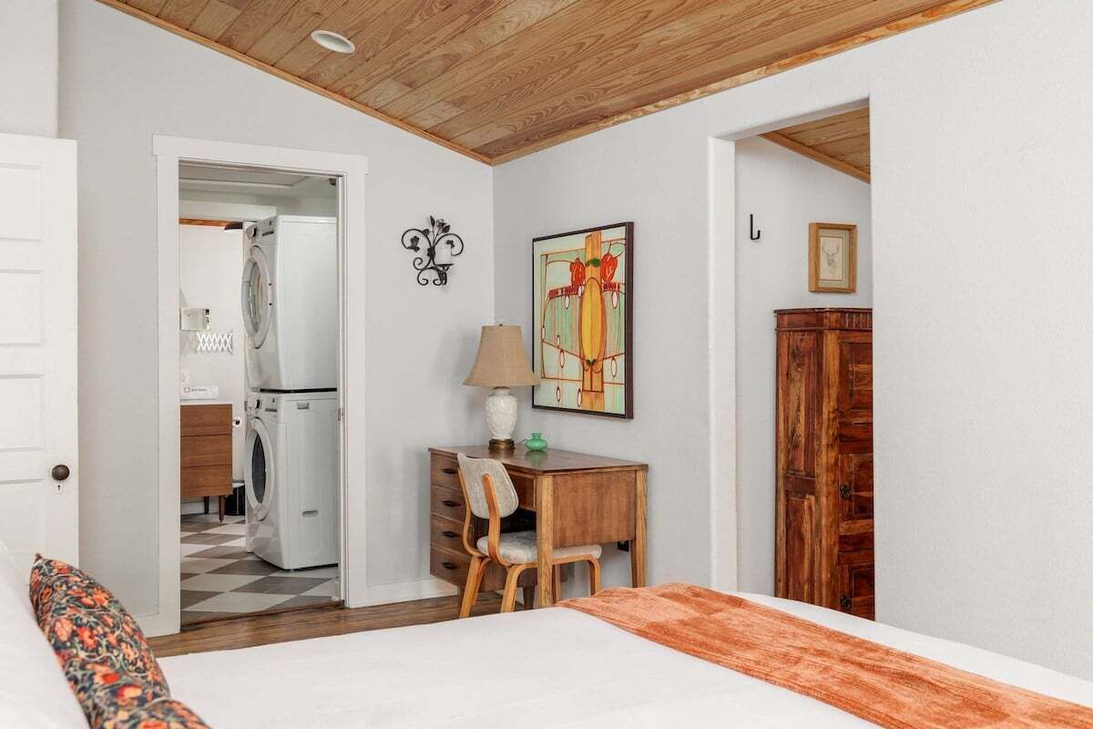 Una camera da letto con un letto, una scrivania e una sedia. Si apre una porta che dà su un bagno con una lavatrice.