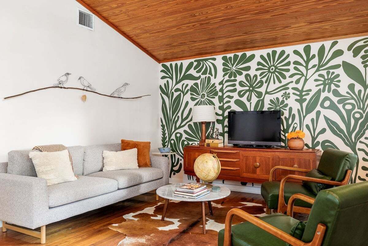 Un salon avec un canapé gris, un meuble en bois sur lequel est posée une télévision, et des fauteuils verts.