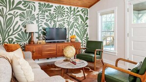 Een woonkamer met een houten plafond, een groen patroonbehang, een televisie op een houten kast, een wereldbol en een groene fauteuil.