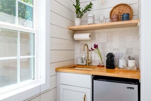 A kitchen with white cabinetry, a wooden countertop, a stainless steel dishwasher, and a window with a view of trees. - Prime East Side Austin - Casa & Casita Cherico (Austin)