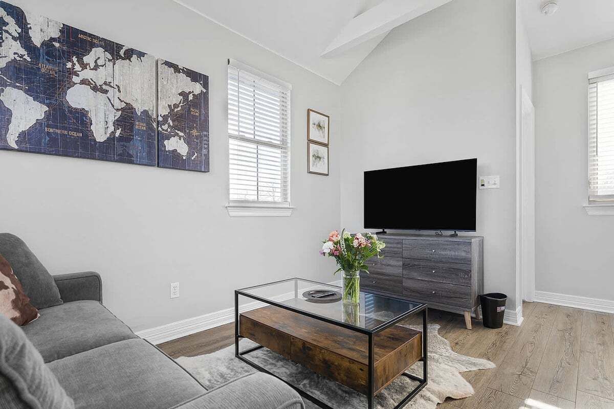 A modern living room with a gray sofa, a glass coffee table with a wooden base, a flat-screen TV on a wooden cabinet, and a world map artwork on the wall.