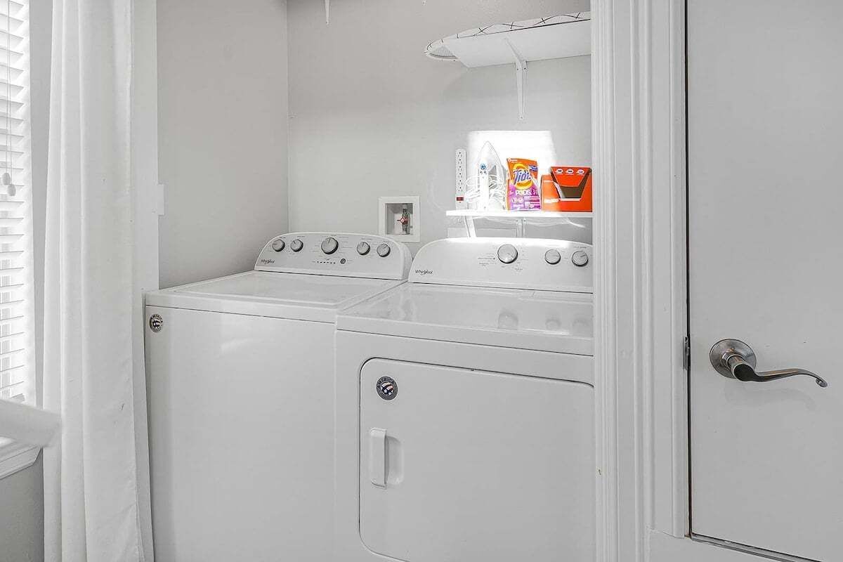 A laundry room with two stacked washers and dryers, a shelf with detergent bottles, and a door with a handle.