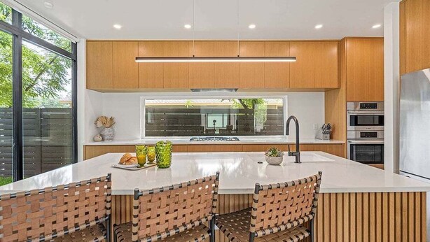 A modern kitchen with wooden cabinets, a large window, and a central island with bar stools.