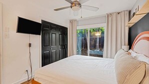 Un dormitori amb un llit, un ventilador de sostre, un televisor fixat a la paret i una porta corredissa de vidre que dona a un espai exterior.
