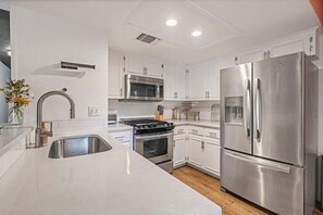 A modern kitchen with white cabinetry, stainless steel appliances, and a central island. - La Casa Chic | Fenced Backyard, Cornhole, 1 Block to South Lamar (Austin)