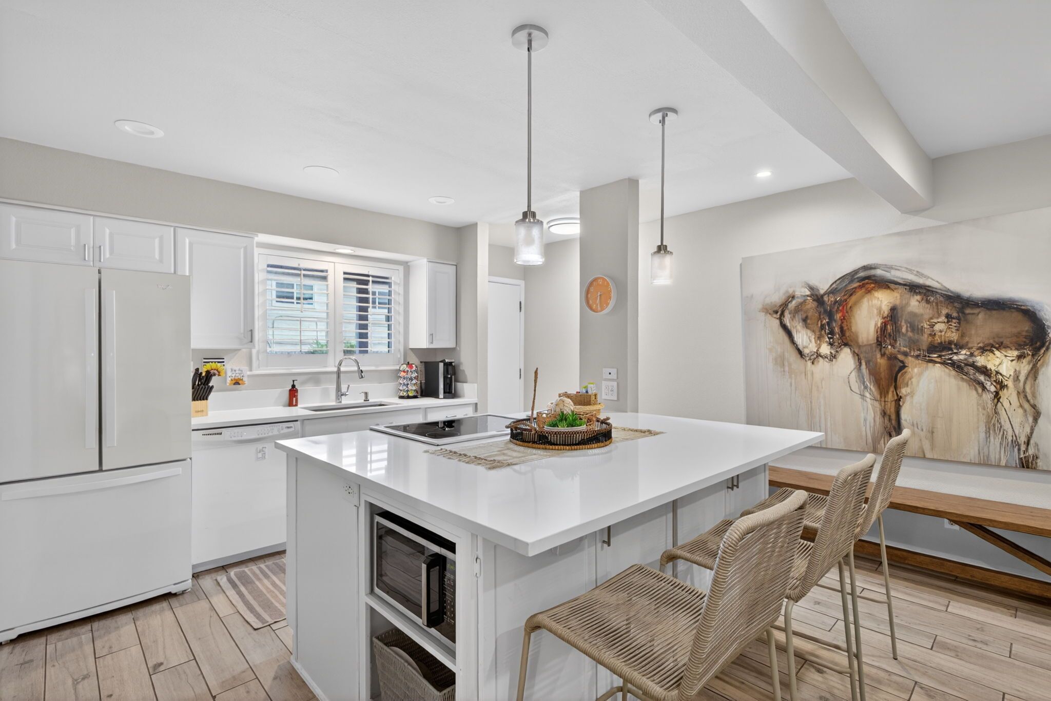 A modern kitchen with white cabinetry, a central island, and a dining area with wicker chairs.