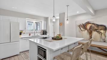 A modern kitchen with white cabinetry, a central island, and a dining area with wicker chairs.