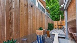 Una valla de madera, plantas en macetas, un sendero de piedra y mobiliario exterior.