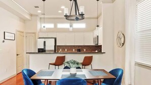 Cocina moderna con armarios blancos, encimera negra y una isla central. Hay una zona de comedor con una mesa y sillas azules.