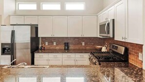 Una cocina con armarios blancos, un refrigerador de acero inoxidable, un microondas y una estufa a gas.