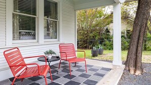 A covered porch with two red metal chairs and a small round table, white siding, and a tree. - Free Parking, Walk to Food - Pastel (Austin)