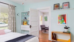 A bedroom with a bed, a bookshelf, a chair, and a small table with books and a plant. - Free Parking, Walk to Food - Pastel (Austin)