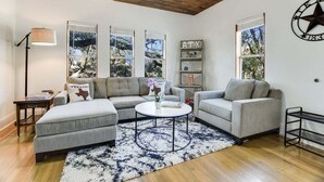 A living room with a sectional sofa, a coffee table, and a bookshelf. - 🌿 SoCo Retreat by Creek with Workspace | Creekside Bungalow 🎶 (Austin)