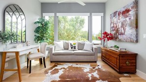 Un salon moderne avec un canapé, un bureau en bois, un tapis en peau de vache et un grand tableau abstrait.