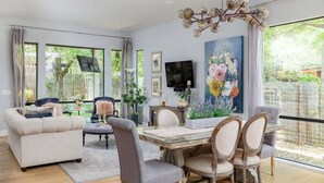 Un salon moderne avec un coin repas, de grandes fenêtres et un lustre.