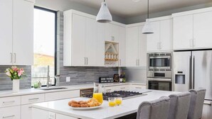 Une cuisine moderne avec des meubles blancs, un îlot central doté de sièges, un four encastré et un réfrigérateur en acier inoxydable.