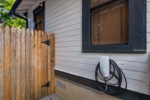 A house with a wooden picket fence, a window with blinds, and a solar panel charger plugged in. - 🔥 Urban Charm · East Austin · Walk to BBQ · Fire Pit & EV Charger ⚡ (Austin)