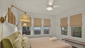 Ein Schlafzimmer mit einem Bett, einem Nachttisch, einer Bank, einem Deckenventilator und Fenstern mit Jalousien.