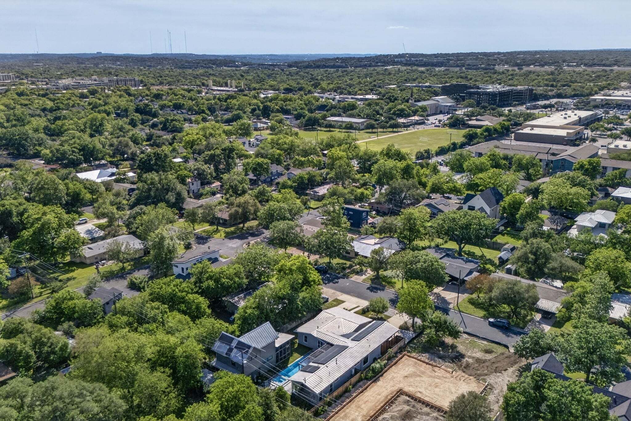 Vue aérienne d’un quartier résidentiel avec des maisons, des arbres et un grand bâtiment doté d’un toit plat.
