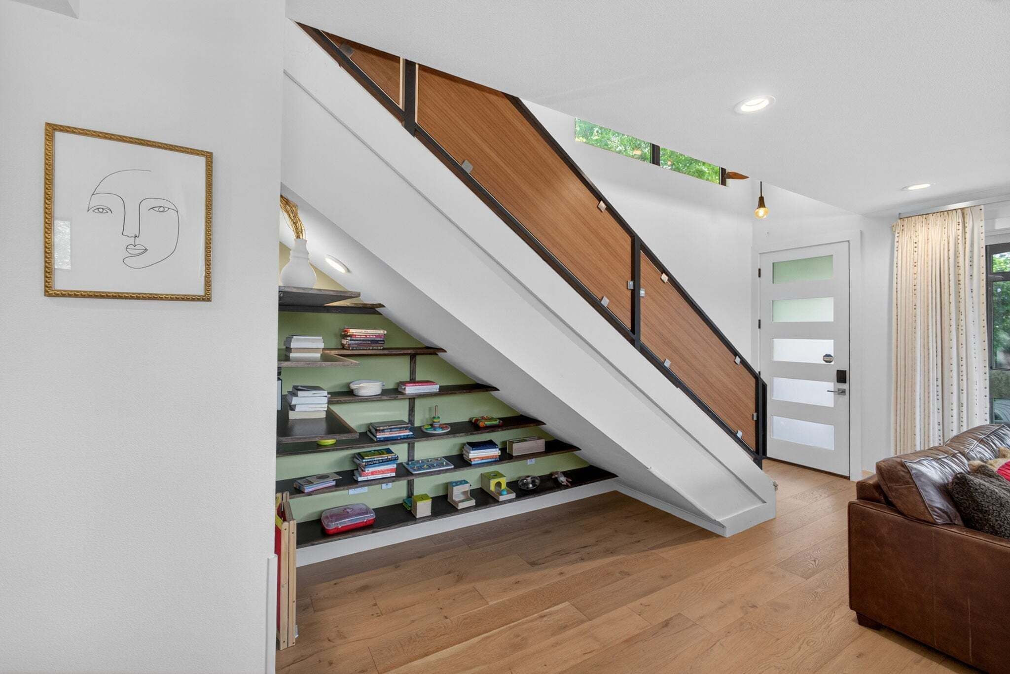 A staircase with wooden steps and a white handrail, leading to a landing with a green shelf holding books and decorative items.