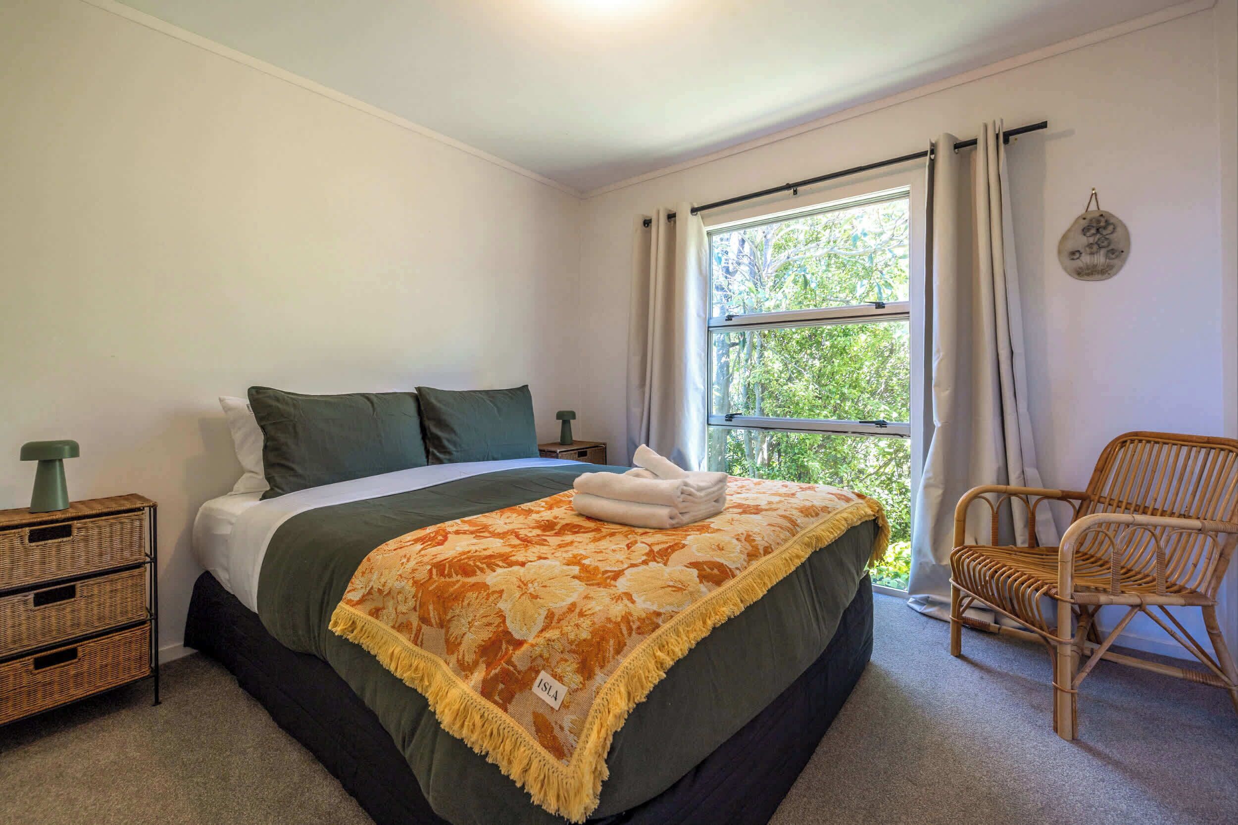 A bedroom with a bed, a chair, a nightstand, and a window with curtains.