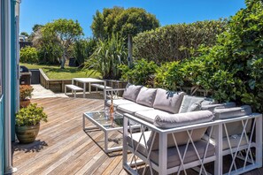 A wooden deck with a white sofa, a glass table, and a barbecue grill.