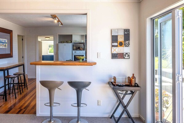A modern kitchen with a bar area, wooden bar stools, and a glass door leading to a balcony.
