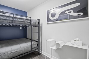 Una cama litera con una pared azul de acento, una mesita de noche blanca con una caja de pañuelos y una obra de arte abstracta enmarcada.