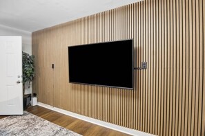 Une pièce avec un téléviseur à écran plat fixé sur un mur composé de lattes de bois, une porte blanche et une plante.