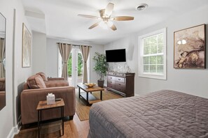 Habitación de hotel con cama, sofá, mesita, televisión, cómoda y ventilador de techo.