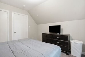A bedroom with a bed, a dresser, a television, and a trash can.