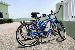 Una bicicleta azul estacionada sobre grava junto a un edificio con valla blanca.