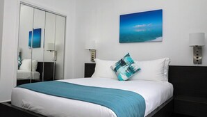 Habitación de hotel con cama, un espejo grande, una mesita de noche, una lámpara de pared y un cuadro de un paisaje marino.