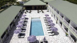 Area piscina con lettini e ombrelloni, circondata da edifici con tetti verdi.