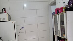 Una cocina con paredes de azulejos blancos, microondas, estufa y refrigerador. Se observa un mueble con puertas de vidrio que contiene diversos utensilios de cocina.