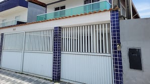 Un edificio de dos pisos con fachada blanca, balcón con azulejos azules y entrada protegida por una reja.