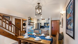 Comedor con una mesa de madera preparada para cuatro personas, una escalera y una cocina al fondo.